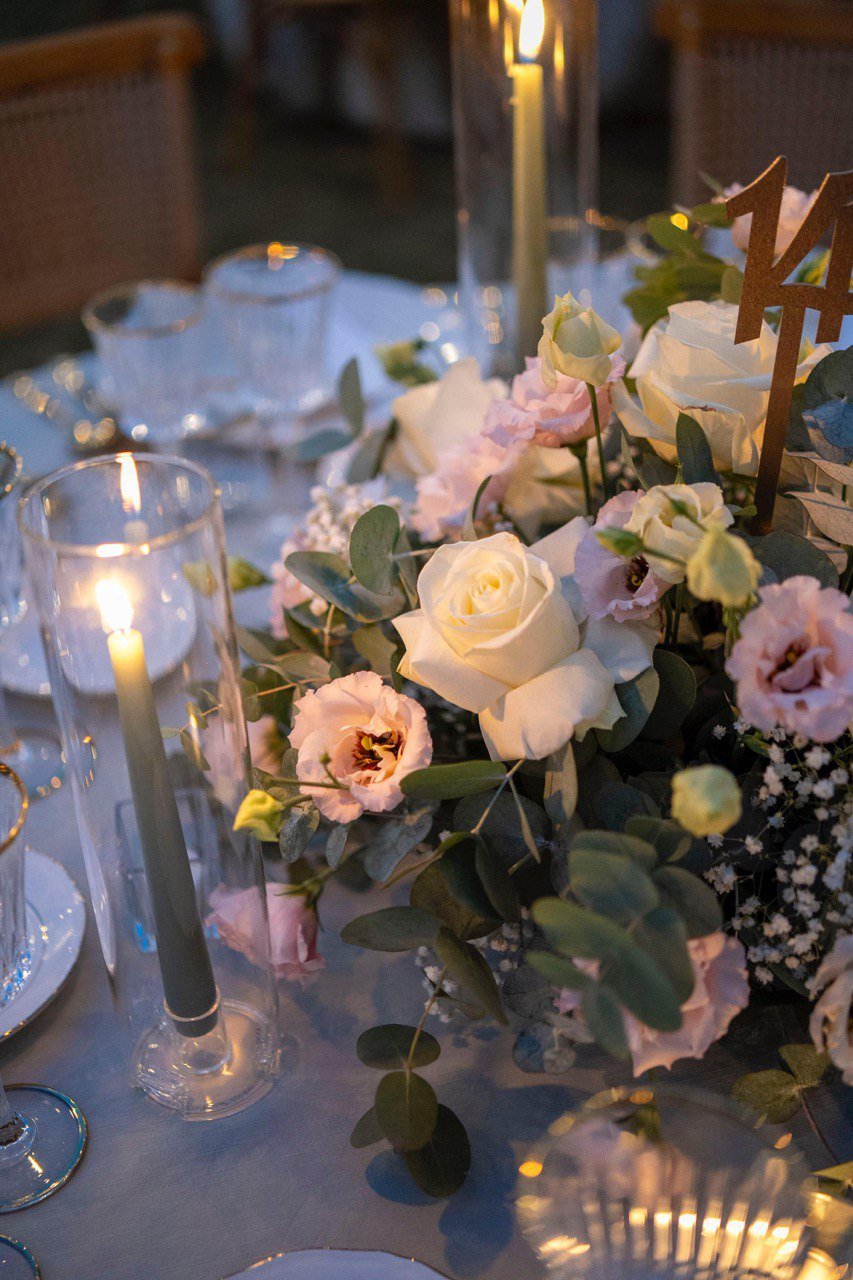 Centro tavola per ricevimento di nozze con rose bianche, lisianthus rosa e candele